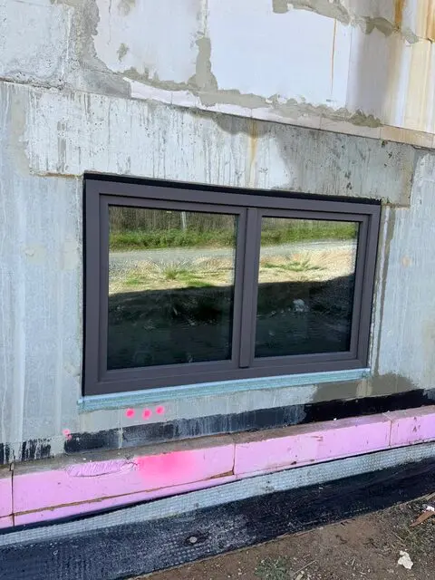 Neu eingebautes Kellerfenster mit dunklem Rahmen und Abdichtung